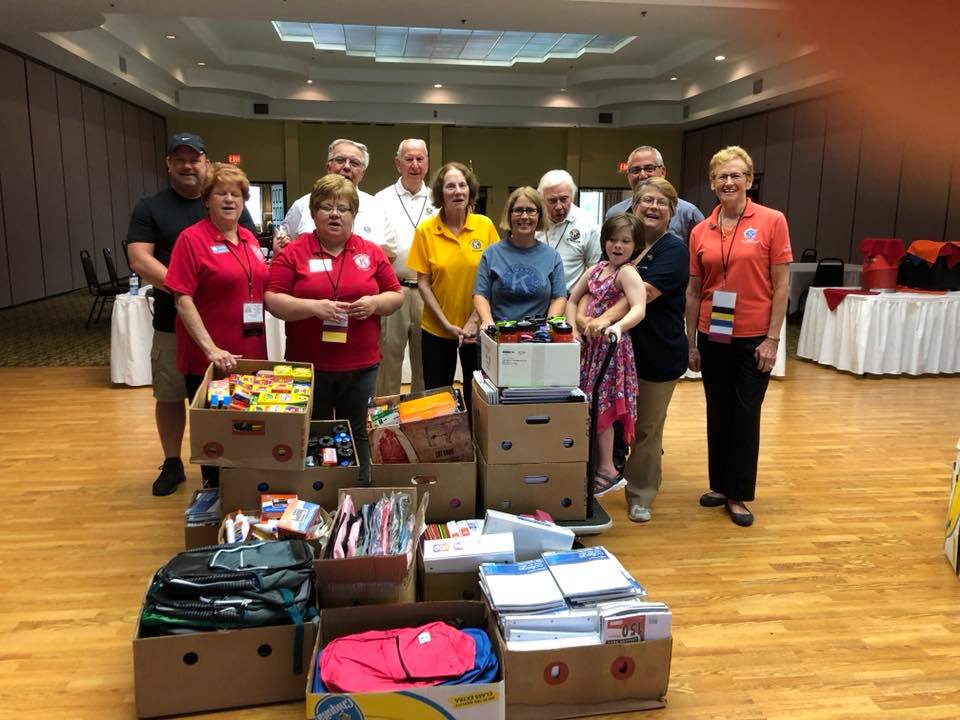 Kiwanis members standing behind several cardboard boxes filled with school supplies